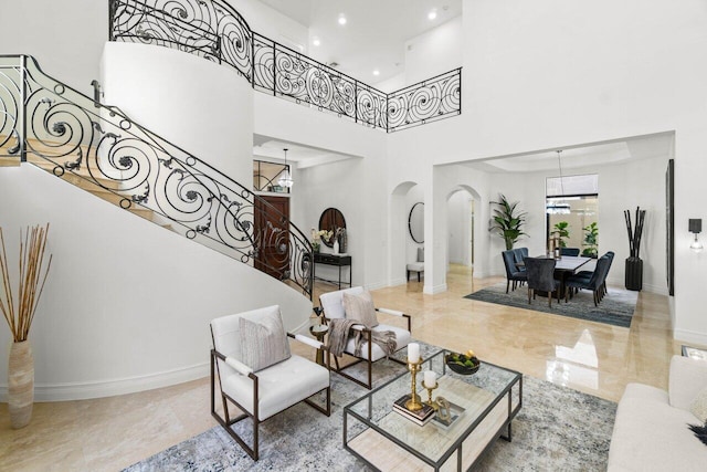 living area with baseboards, arched walkways, an inviting chandelier, a high ceiling, and stairs