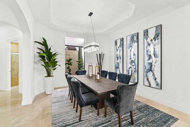 dining room featuring arched walkways, a tray ceiling, an inviting chandelier, and baseboards