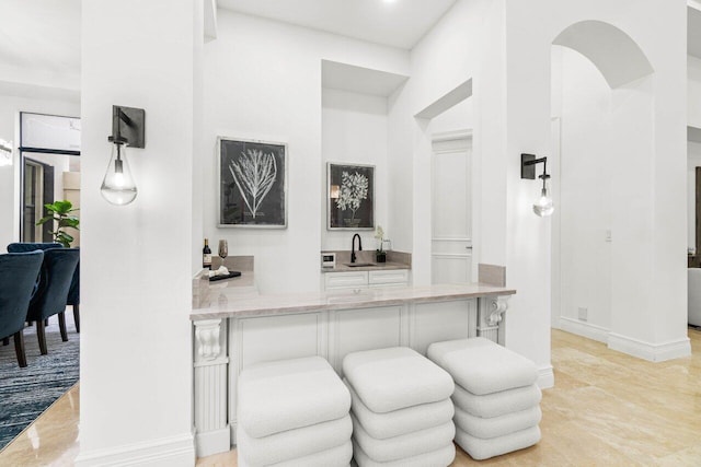 bar featuring baseboards, arched walkways, and a sink