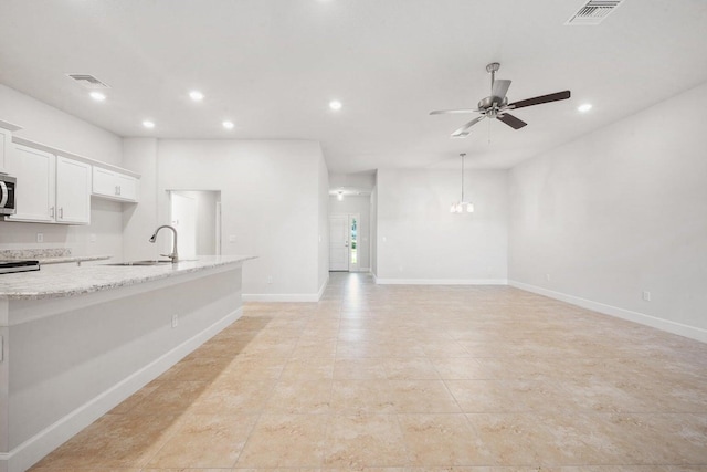 kitchen with light stone counters, ceiling fan, sink, pendant lighting, and white cabinetry