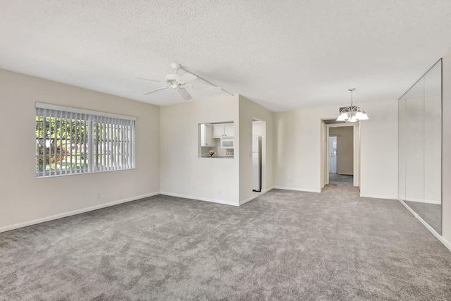 spare room with carpet flooring, ceiling fan with notable chandelier, and a textured ceiling