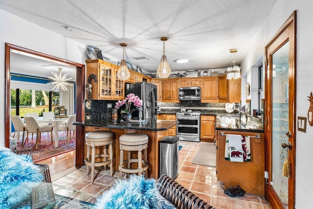 kitchen with backsplash, kitchen peninsula, decorative light fixtures, a breakfast bar area, and appliances with stainless steel finishes