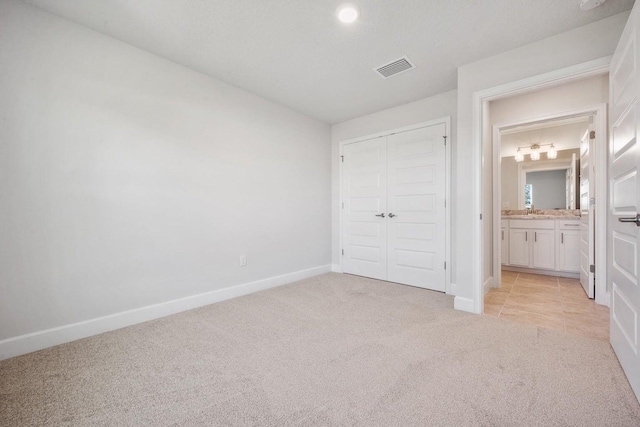 unfurnished bedroom with light carpet, a closet, and ensuite bathroom