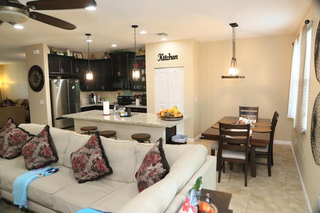 kitchen with light stone countertops, an island with sink, black appliances, and decorative light fixtures