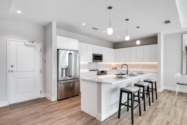 kitchen featuring a center island with sink, white cabinets, light wood-type flooring, and appliances with stainless steel finishes