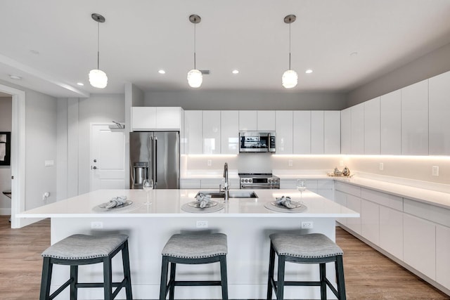 kitchen with white cabinets, a kitchen island with sink, sink, and appliances with stainless steel finishes