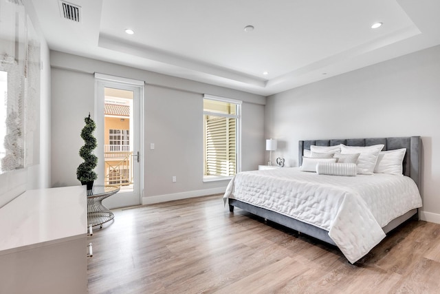 bedroom featuring a tray ceiling, access to exterior, and light hardwood / wood-style flooring