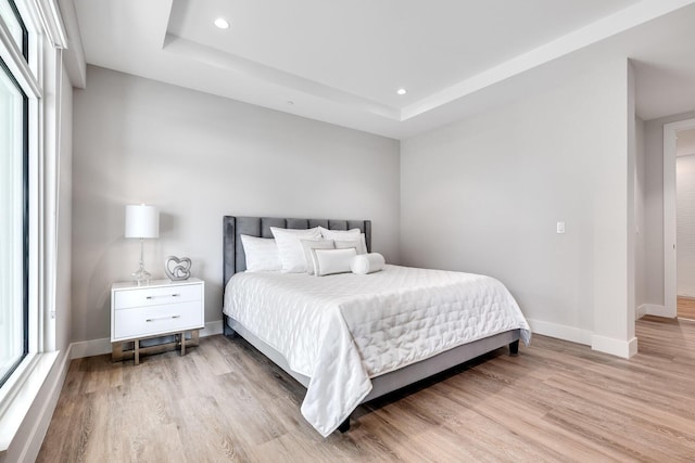 bedroom with a raised ceiling and light hardwood / wood-style floors