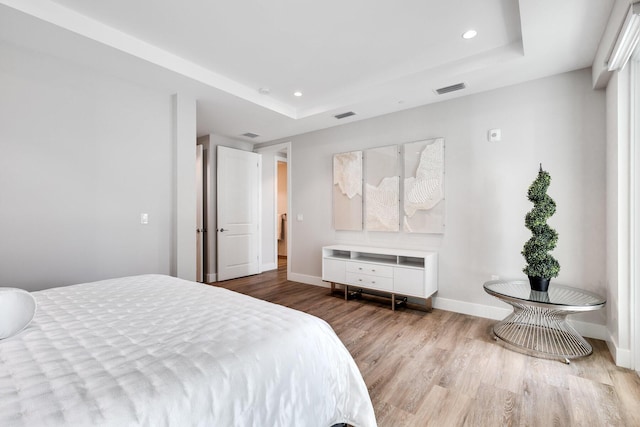 bedroom featuring a raised ceiling and light wood-type flooring