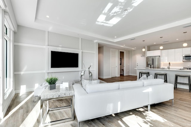 living room featuring a raised ceiling, sink, and light hardwood / wood-style floors