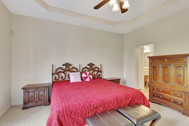 carpeted bedroom with ceiling fan, a raised ceiling, and ensuite bath