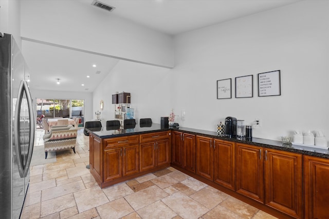 kitchen with stainless steel refrigerator, kitchen peninsula, dark stone counters, and vaulted ceiling