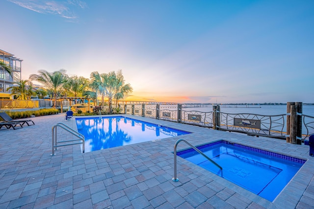 pool at dusk with a community hot tub, a water view, and a patio area