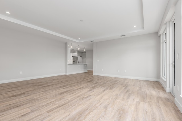 unfurnished living room with light hardwood / wood-style floors and a raised ceiling