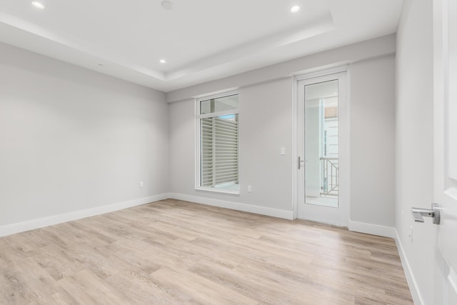 empty room featuring a tray ceiling and light wood-type flooring