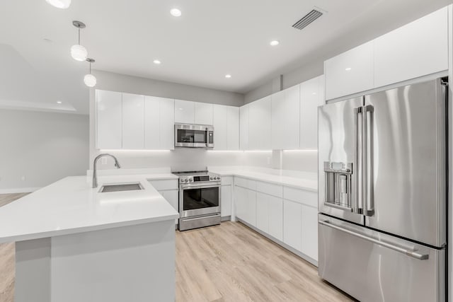 kitchen featuring appliances with stainless steel finishes, light wood-type flooring, sink, decorative light fixtures, and white cabinetry