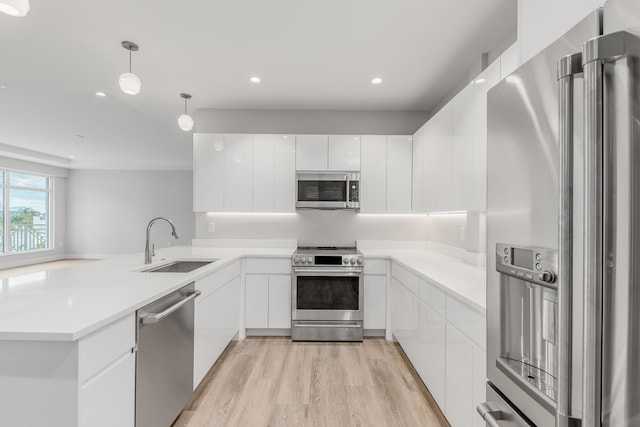 kitchen with hanging light fixtures, sink, light hardwood / wood-style flooring, appliances with stainless steel finishes, and white cabinetry