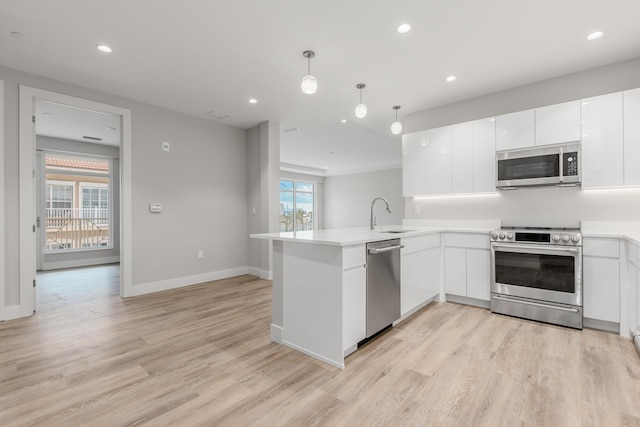 kitchen featuring kitchen peninsula, appliances with stainless steel finishes, sink, light hardwood / wood-style floors, and hanging light fixtures