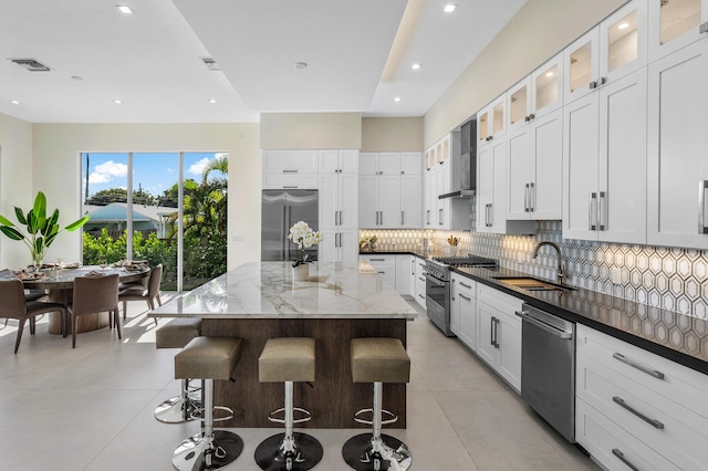 kitchen with wall chimney exhaust hood, stainless steel appliances, sink, white cabinetry, and a kitchen island