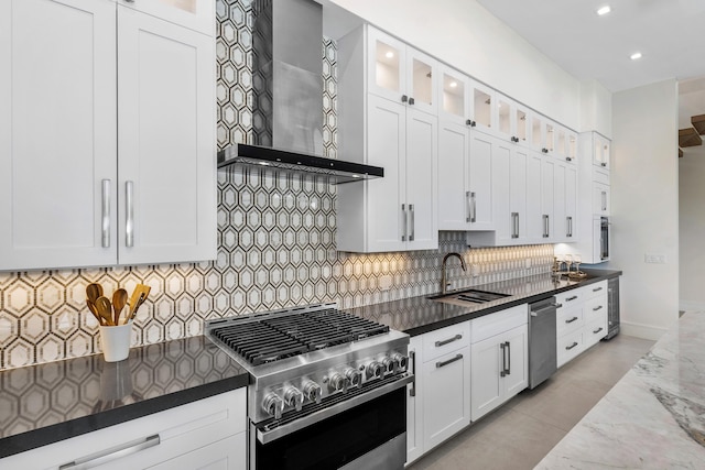 kitchen with high end range, wall chimney exhaust hood, sink, dark stone countertops, and white cabinetry