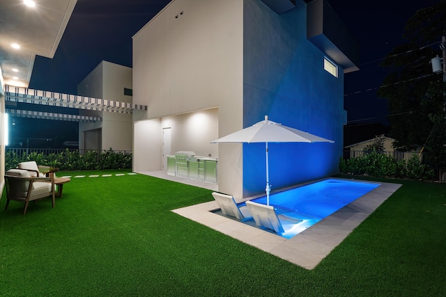 pool at night with a yard and an outdoor kitchen