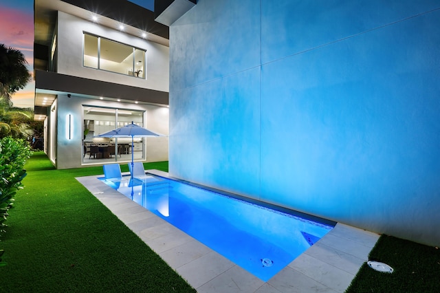 pool at dusk featuring a yard and a patio