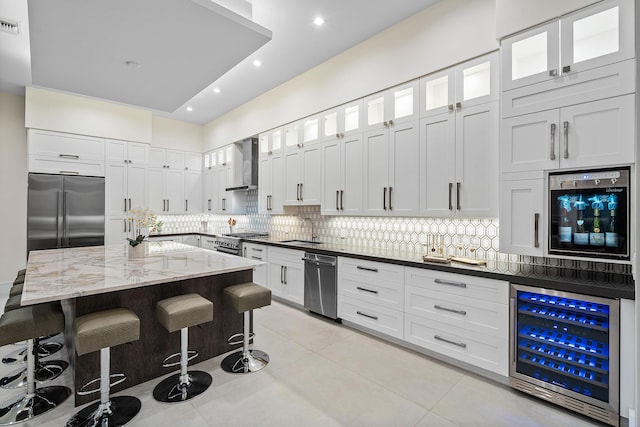 kitchen featuring appliances with stainless steel finishes, beverage cooler, wall chimney range hood, white cabinets, and a center island