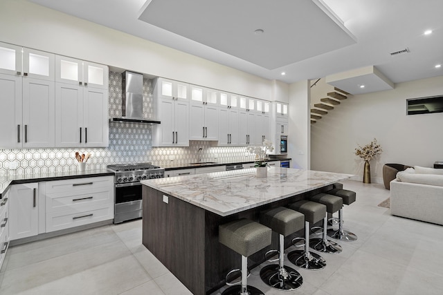 kitchen featuring white cabinets, a kitchen island, wall chimney range hood, and high end stainless steel range