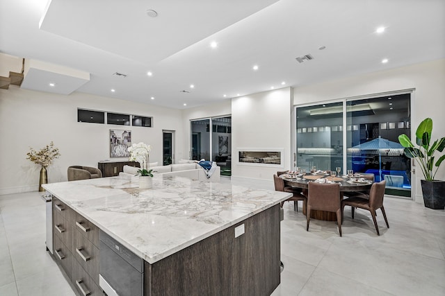 kitchen with built in microwave, a large island, dark brown cabinets, and light stone counters