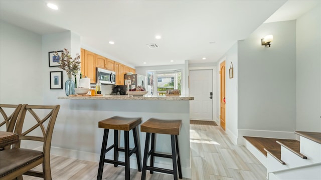 kitchen featuring a kitchen bar, appliances with stainless steel finishes, kitchen peninsula, light stone counters, and light hardwood / wood-style flooring