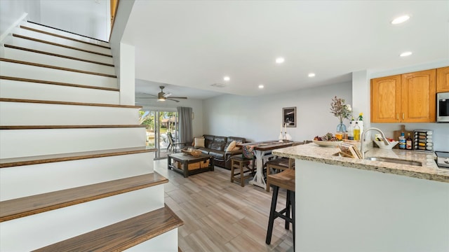 kitchen featuring light wood-type flooring, light stone counters, ceiling fan, sink, and a breakfast bar area