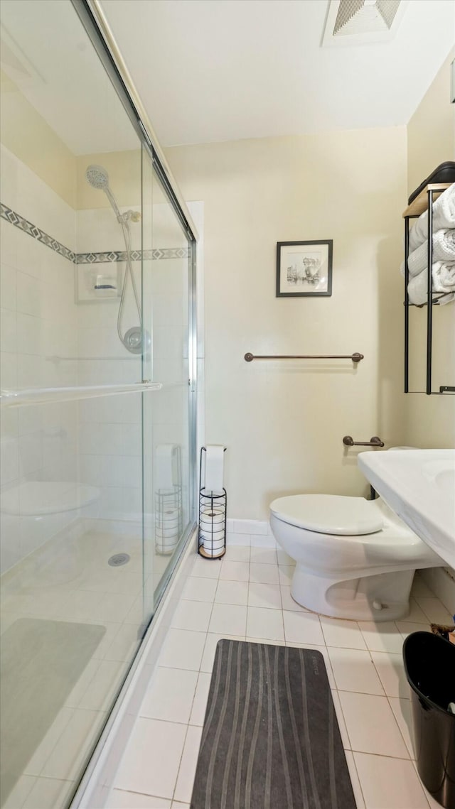 bathroom with tile patterned floors, toilet, and a shower with door