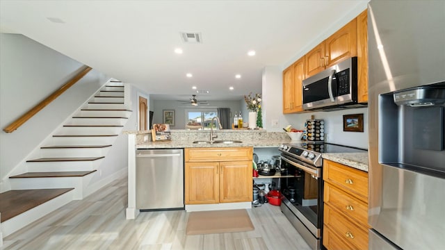 kitchen featuring kitchen peninsula, light stone counters, stainless steel appliances, ceiling fan, and sink