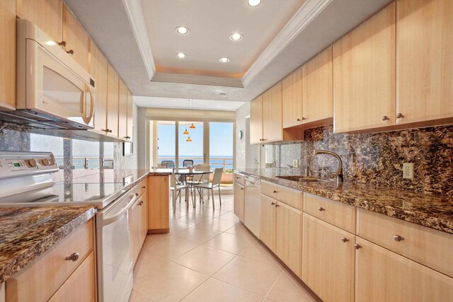 kitchen featuring sink, white appliances, a tray ceiling, light brown cabinetry, and a water view