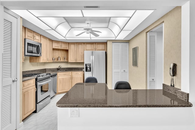 kitchen with ceiling fan, light brown cabinets, kitchen peninsula, dark stone counters, and appliances with stainless steel finishes