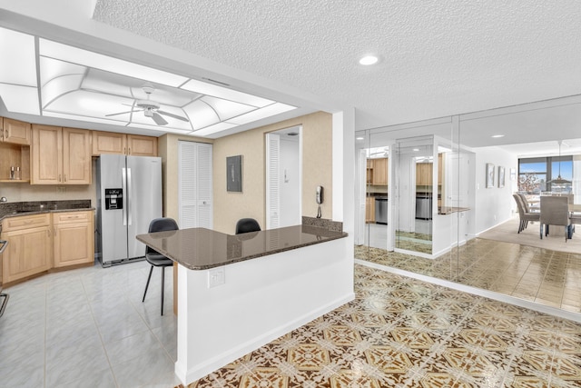 kitchen with stainless steel refrigerator with ice dispenser, a kitchen breakfast bar, a textured ceiling, ceiling fan, and light brown cabinets