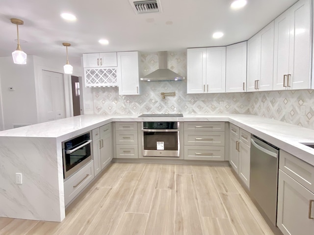 kitchen with light stone counters, stainless steel appliances, visible vents, wall chimney range hood, and pendant lighting