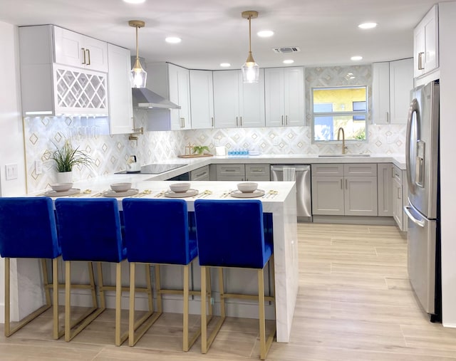 kitchen with visible vents, a sink, stainless steel appliances, a peninsula, and wall chimney exhaust hood