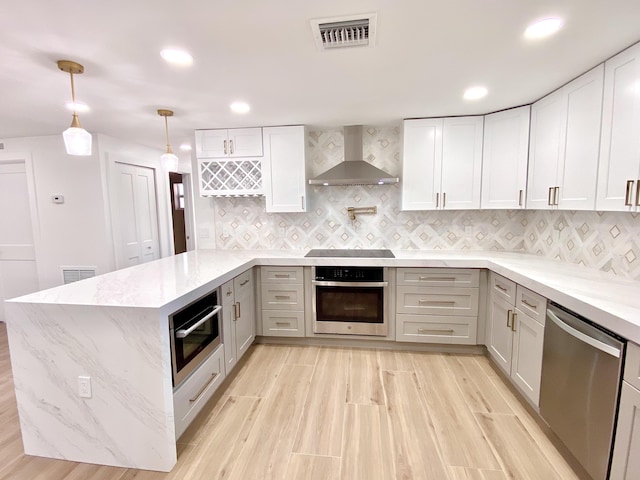 kitchen featuring a peninsula, wall chimney exhaust hood, visible vents, and stainless steel appliances