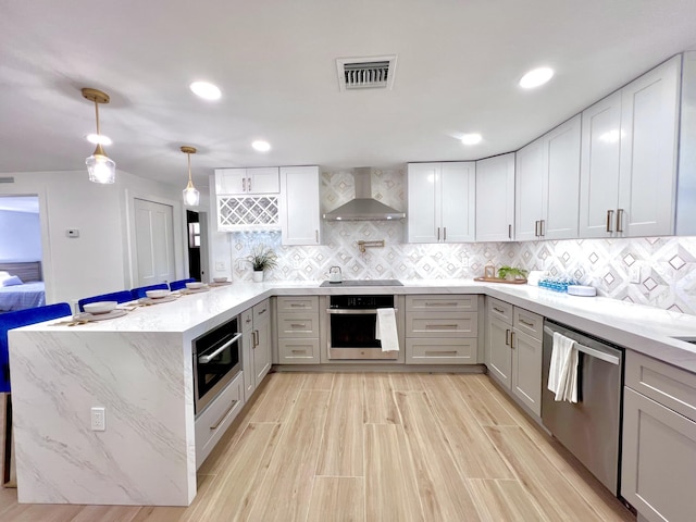 kitchen featuring visible vents, backsplash, wall chimney range hood, appliances with stainless steel finishes, and a peninsula