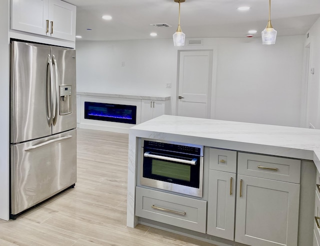 kitchen with decorative light fixtures, stainless steel appliances, visible vents, gray cabinetry, and a glass covered fireplace