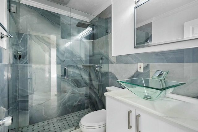 bathroom featuring crown molding, toilet, vanity, a shower with shower door, and tile walls