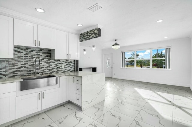 kitchen with pendant lighting, sink, kitchen peninsula, decorative backsplash, and white cabinetry