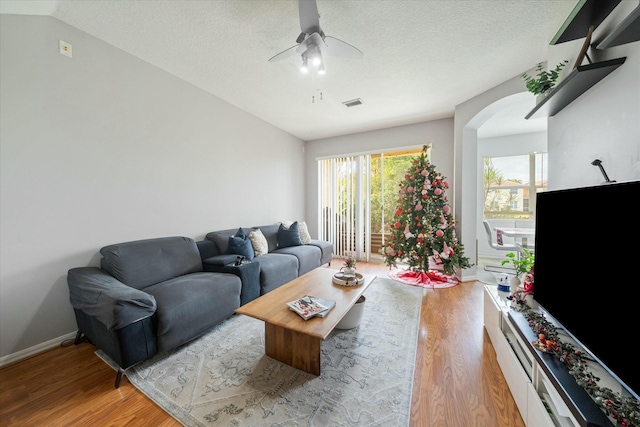 living room featuring ceiling fan, light wood-type flooring, a textured ceiling, and vaulted ceiling