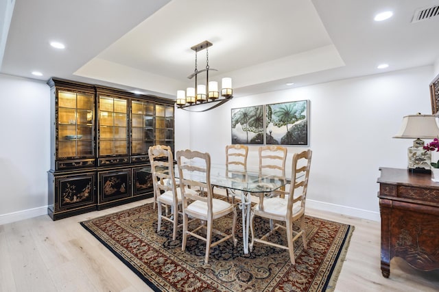 dining room featuring an inviting chandelier, light hardwood / wood-style floors, and a raised ceiling