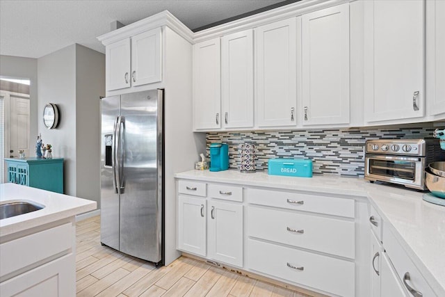 kitchen featuring stainless steel fridge, light wood-type flooring, white cabinetry, and a textured ceiling