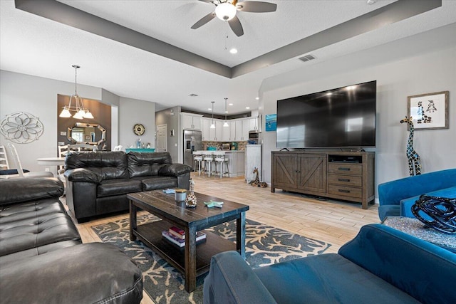 living room with a textured ceiling, ceiling fan with notable chandelier, and light wood-type flooring