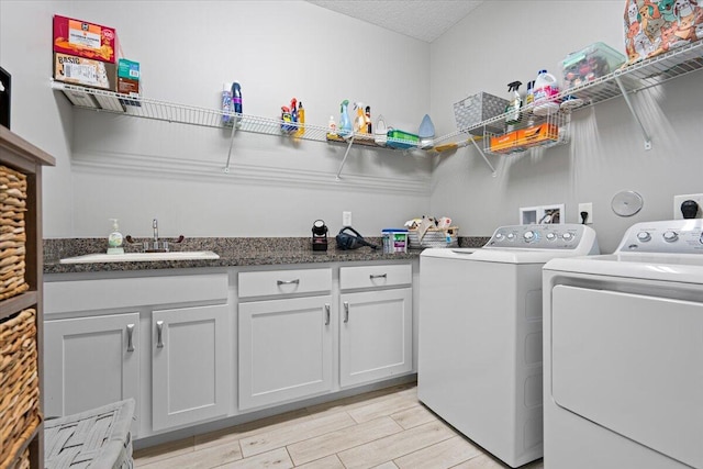 laundry area featuring cabinets, a textured ceiling, sink, light hardwood / wood-style flooring, and washing machine and clothes dryer