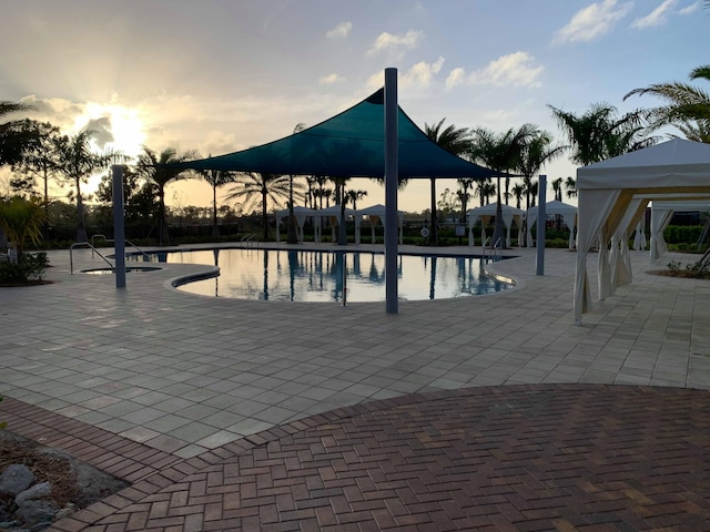 pool at dusk featuring a gazebo and a patio