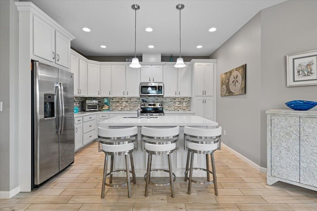 kitchen featuring white cabinets, pendant lighting, stainless steel appliances, and an island with sink